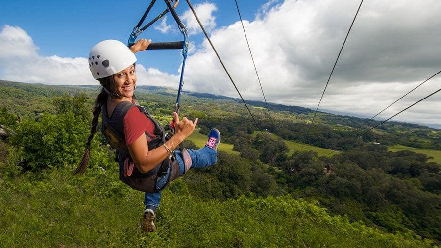 A woman is hanging on to the ropes of a zip line.