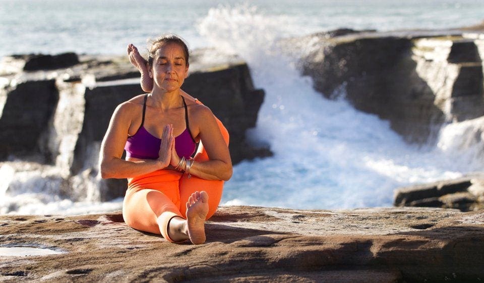 A woman sitting on the beach doing yoga.