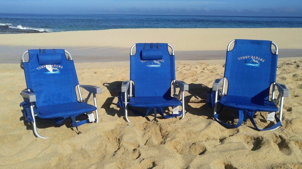 Three lawn chairs on the beach in front of a body of water.
