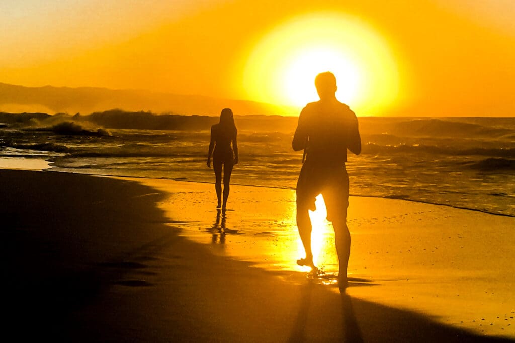 A man and woman walking on the beach at sunset.